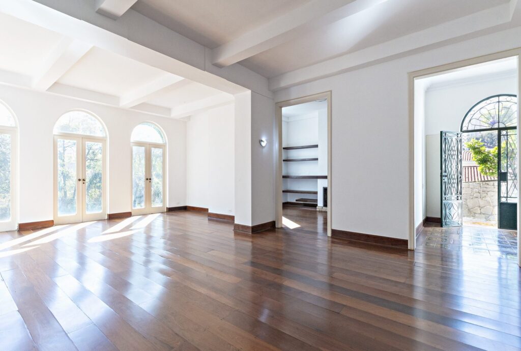 Foto da sala de uma casa, com piso de madeira e amplas janelas.