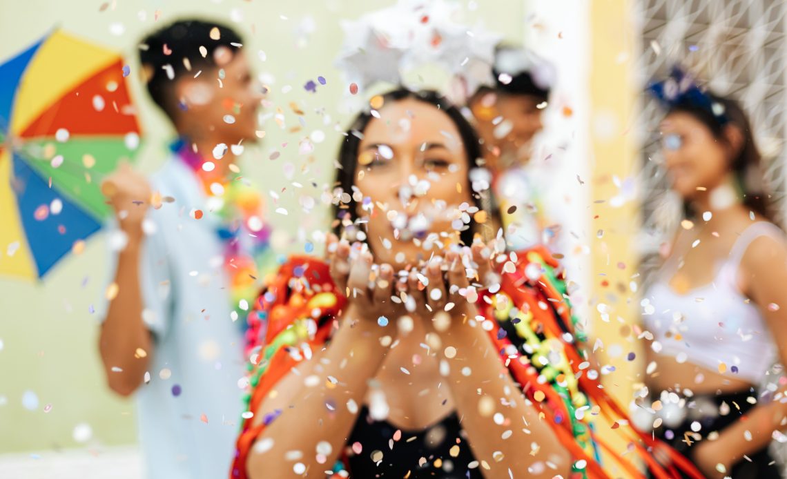 Mulher assoprando confete com roupa colorida em bloco de carnaval